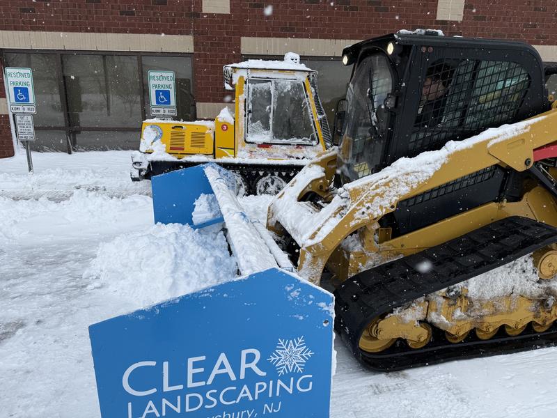 Skid steer with a Clear Landscaping pusher working a tight commercial area