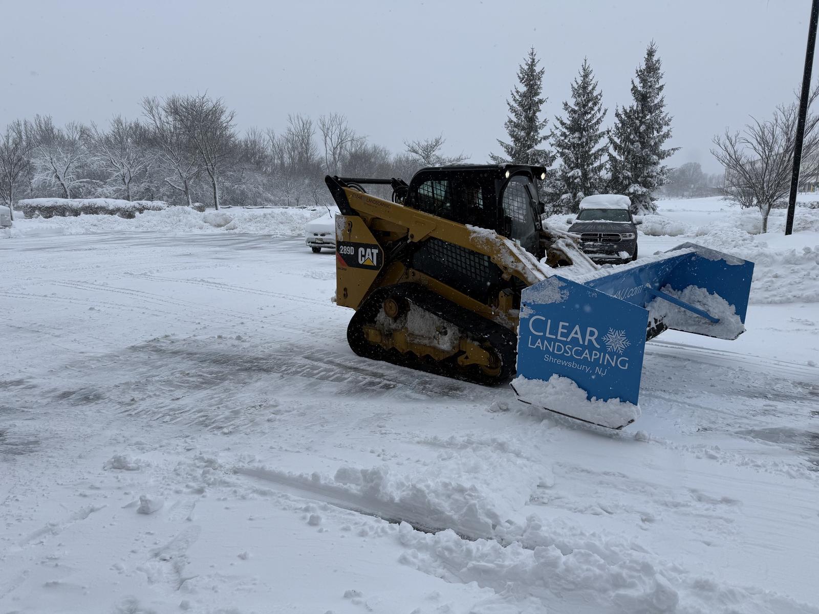 A Clear Landscaping wheel loader clearing a commercial parking lot at night during a snow event